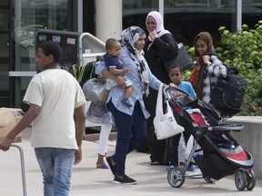 Refugee families carry luggage to an awaiting van at Humber College to take them to new temporary accommodations at a Radisson Hotel in Toronto, on Aug. 9, 2018.