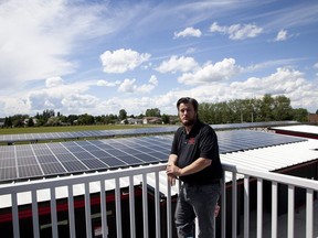 Greg Robinson poses in front of solar panels on top of a municipal building in Raymond, Alta., in this recent handout photo. What began as a little friendly rivalry between two nearby southern Alberta towns has ended with what may be the most extensive program of solar power anywhere in the country. Since the fall, Raymond, Alta., has operated nine municipal buildings and all of its streetlights by the sun, selling excess solar power to the electrical grid when it can and buying it back when it can't. It's become Alberta's first "net zero" community.