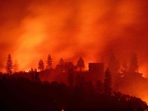 In this file photo taken on November 10, 2018 flames from the Camp fire burn near a home atop a ridge near Big Bend, California. - The US Congress overcame months of delays to finally pass a $19.1 billion relief package June 3, 2019, to help victims of flooding, wildfires and hurricanes that have devastated communities from Puerto Rico to California.