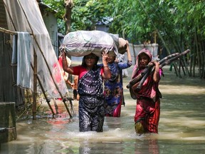Bangladeshi women carry their belongings as they wade through flood waters following heavy mosoon rains in Kurigram on July 17, 2019. - In flood-prone Bangladesh, which is criss-crossed by rivers, around one-third of the country is underwater and people were being killed by lightning strikes, officials said