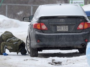 A police officer looks for evidence under a car in the area of a shooting at a Quebec City mosque on Monday Jan. 30, 2017.