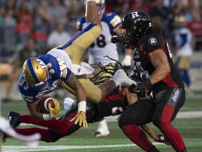 Ottawa Redblacks defensive lineman J.R. Tavai, right, looks on as Winnipeg Blue Bombers running back Andrew Harris, left, is upended by defensive back Sherrod Baltimore during second quarter CFL action in Ottawa, Friday, July 5, 2019.