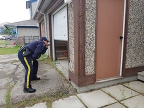 An RCMP officer shines a light into an open garage at a home in the Gillam, Man., area in July 27, 2019, police image published to social media.
