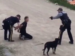 A northern Saskatchewan RCMP officer pointing his gun during an arrest. He has been relocated as the RCMP investigates his conduct caught on two videos. (Facebook/screengrab)