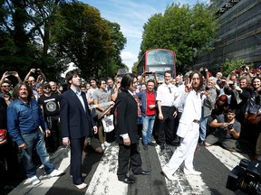 People take pictures as the Beatles cover band members walk on the zebra crossing on Abbey Rod. in London, England, Aug. 8, 2019.