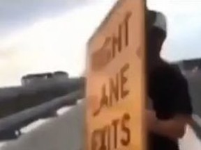 A screengrab from a video posted to Reddit of a young man throwing a sign onto the QEW in Oakville.