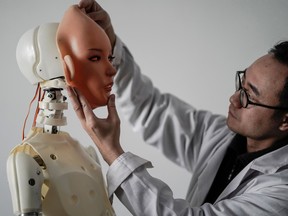 This photo taken on February 1, 2018 shows an engineer holding a silicon face against the head of a robot at a lab of a doll factory of EXDOLL, a firm based in the northeastern Chinese port city of Dalian. With China facing a massive gender gap and a greying population, a company wants to hook up lonely men and retirees with a new kind of companion: "Smart" sex dolls that can talk, play music and turn on dishwashers.