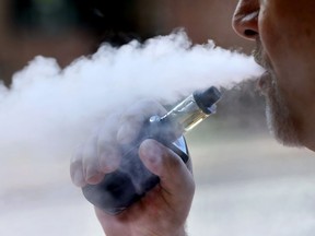 In this Aug. 28, 2019 photo a man exhales while smoking an e-cigarette in Portland, Maine. Health Canada says people who vape should get medical attention right away if they're worried their electronic cigarettes are harming them.