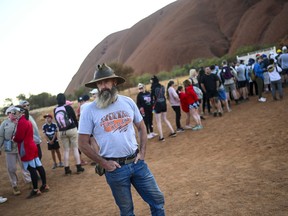 A man wearing a T-shirt saying "I chose not to climb" stands next to tourists lining up to climb Uluru, formerly known as Ayers Rock, at Uluru-Kata Tjuta National Park in the Northern Territory, Australia, October 25, 2019. (AAP Image/Lukas Coch/via REUTERS)