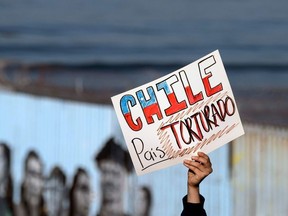 A person holds a sign that reads 'Chile, tortured country' during a demonstration to support Chile's protests and against the Chilean President near the US-Mexico border in Playas de Tijuana, Baja California state, Mexico, on October 24, 2019.