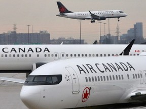 Two Air Canada Boeing 737 Max 8 aircrafts are seen on the ground as Air Canada Embraer aircraft flies in the background at Pearson International Airport in Toronto, March 13, 2019.