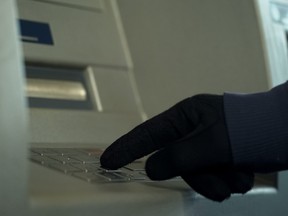 Mans hand in gloves inserting pin code, stealing money from bank account, atm