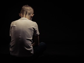 Rear View of a Seated Sad Young Boy Against Black