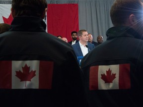 Conservative staff members wearing jackets with the Canadian flag on them look on as Conservative leader Andrew Scheer addresses the media during a morning announcement during a campaign stop in Toronto Friday, Oct.  4, 2019.