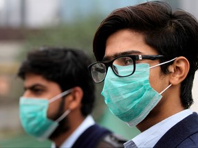 Men wearing protective masks wait for a bus in Lahore, Pakistan Nov. 22, 2019. REUTERS/Mohsin Raza