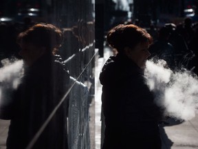 A woman exhales while smoking a vaporizer outside an office tower in downtown Vancouver, Tuesday, Feb. 28, 2017.