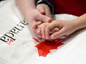 A mother holds the hands of her daughter as they become new Canadians and take the Oath of Citizenship on Parliament Hill in Ottawa on April 17, 2019.