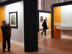 A visitor takes a picture of an artwork as a woman walks past the painting "Crucifix" by Salvador Dali during an exhibition of delicate works on paper at the Vatican, December 11, 2019.