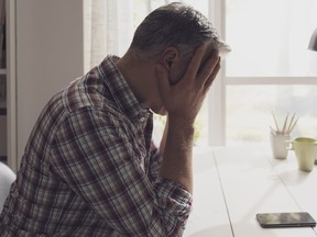 Desperate man waiting for a phone call at home, he is staring at the phone with head in hands