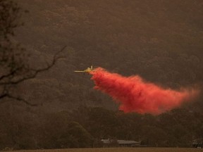A small aircraft dumps fire retardant behind houses at the foot of Mount Tennant as the fire front of the Orroral Valley fire creeps through the Namadgi National Park on January 30, 2020 in Canberra, Australia. Firefighters are on high alert as heatwave conditions in New South Wales and the ACT increase the fire danger across areas which have already been affected by bushfire in recent months.