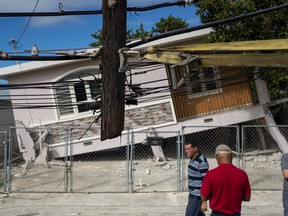 People pass by a house damaged by an earthquake in Guanica, Puerto Rico on Jan. 6, 2020. (RICARDO ARDUENGO/AFP via Getty Images)