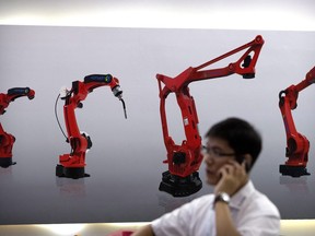 In this Aug. 15, 2018, photo, a visitor talks on his smartphone in front of a display of manufacturing robots from Chinese robot maker Honyen at the World Robot Conference in Beijing, China.