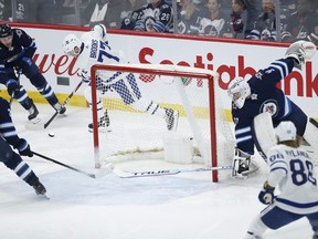 Jets goaltender Connor Hellebuyck (37) gets caught behind the net as Maple Leafs' Adam Brooks (77) steals the puck and passes to William Nylander (88) who takes the shot to score Thursday night in Winnipeg.