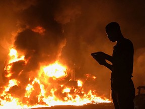 A man stands with his phone in front of flames rising from a pipeline explosion in Abula-Egba, Lagos, Nigeria, Jan. 19, 2020.