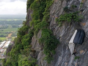 A BASE jumper hangs, snagged from his parachute, after being blown into the Khao Thalu cliff, Khuha Sawan, Mueang Phatthalung District, Thailand January 13, 2020 in this image obtained from social media. Picture taken January 13, 2020.