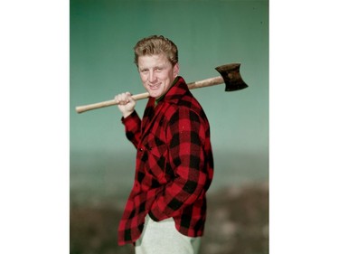 Portrait of American actor Kirk Douglas wearing a black and red checked jacket and holding an axe over his shoulder in the  1950s.