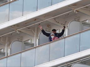 A passenger waves next to another wearing a face mask from the cruise ship Diamond Princess as it is anchored at Daikoku Pier Cruise Terminal in Yokohama, south of Tokyo, Japan Feb. 7, 2020. REUTERS/Kim Kyung-Hoon