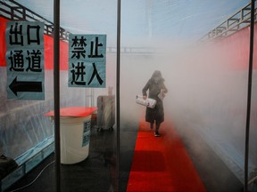 A woman wearing a face mask walks through a device that sprays disinfectant at an entrance to a residential compound, following an outbreak of the novel coronavirus in the country, in Tianjin, China Feb. 11, 2020.  (cnsphoto via REUTERS)