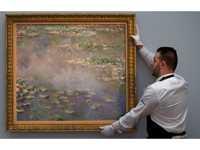 In this file picture taken on June 18, 2014, a Sotheby's employee poses with a painting by late French impressionist painter Claude Monet, entitled 'Nympheas' which was sold at an auction in London on Monday, June 23, 2014.