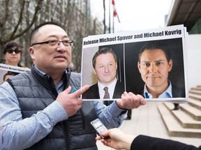 In this file photo taken on March 6, 2019, Louis Huang of Vancouver Freedom and Democracy for China holds photos of Canadians Michael Spavor and Michael Kovrig, who are being detained by China, outside British Columbia Supreme Court, in Vancouver.
