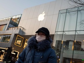 In this file photo taken on Feb. 3, 2020 a woman wearing a protective facemask walks outside of a closed-off Apple Store in Beijing. (NICOLAS ASFOURI/AFP via Getty Images)