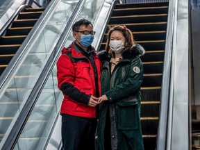 A couple wearing a protective facemask use an escalator outside a nearly empty shopping mall at lunch time in Beijing on February 22, 2020.