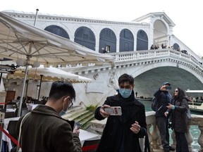 Tourists pose for selfies in front of the Rialto bridge in Venice after the carnival was cancelled due to a coronavirus outbreak in Italy, on Feb. 24, 2020. (ANDREA PATTARO/AFP via Getty Images)