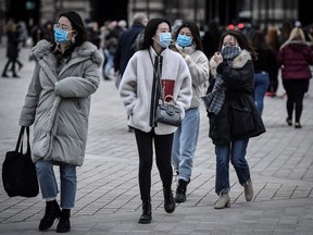 Tourists wearing a protective face mask amid fears of the spread of the COVID-19 novel coronavirus walk at the Pyramide du louvre area on February 28, 2020 in Paris.