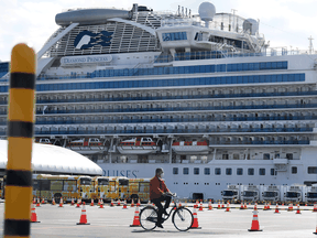 A man cycles past city buses lined up to transport passengers finally disembarking from the Diamond Princess cruise ship — in quarantine due to an outbreak of COVID-19 coronavirus — at the Daikoku Pier Cruise Terminal in Yokohama earlier this month.