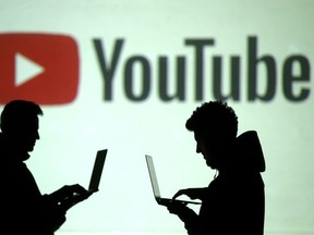 Silhouettes of mobile device users are seen next to a screen projection of YouTube logo in this picture illustration taken March 28, 2018.