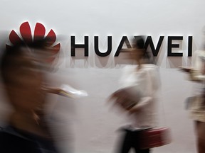 In this file photo taken on August 2, 2019 people walk past a Huawei logo during the Consumer Electronics Expo in Beijing. (FRED DUFOUR/AFP via Getty Images)