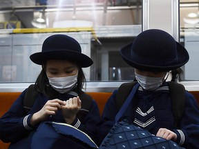 Schoolgirls wearing protective masks travel on a train in Tokyo on February 13, 2020. (CHARLY TRIBALLEAU/AFP via Getty Images)