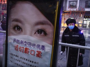 A Chinese security guard wears a protective mask as he waits to take temperatures while standing next to a sign instructing people to wear masks, at a nearly empty commercial street in Beijing, China, on Wednesday, Feb. 12, 2020.