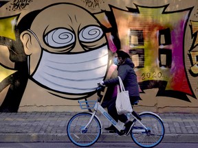 A woman wearing a protective mask cycles past graffiti-painted wall at a construction site in Shanghai, China, as the country is hit by coronavirus outbreak, Feb. 17, 2020.