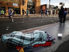 A homeless person sleeps as runners jog past during the Los Angeles Marathon, which was allowed to continue by health officials in spite of coronavirus COVID-19 fears, on March 8, 2020 in Los Angeles, California. L.A.