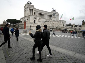 Tourists wearing protective masks walk by the Vittoriano in central Rome, on March 1, 2020.