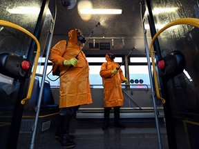 Men wearing protective gear spray disinfectant as part of preventive measures against the spread of the COVID-19 coronavirus, inside a bus at a terminal in Tbilisi on March 2, 2020. (VANO SHLAMOV/AFP via Getty Images)
