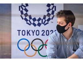 A man wearing a facemask, amid concerns over the spread of the COVID-19 coronavirus, sits at a bus stop in front of a Tokyo 2020 Olympics advertisement in Bangkok on March 16, 2020. (Photo by Mladen ANTONOV / AFP)