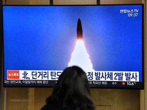 A woman watches a television news broadcast showing a file image of a North Korean missile test, at a railway station in Seoul on March 21, 2020.