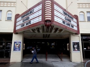 A pedestrian walks under the marquee at Balboa Theater that notes the theater is closed until further notice due to a statewide ordinance banning gatherings of more than 250 people, in San Francisco, Sunday, March 15, 2020.